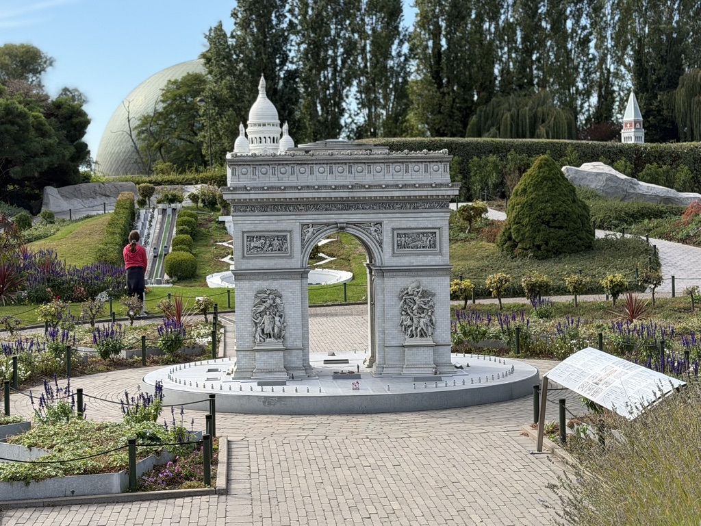 L’Arc de Triomphe miniature entouré de parterres fleuris, avec le Sacré-Cœur derrière