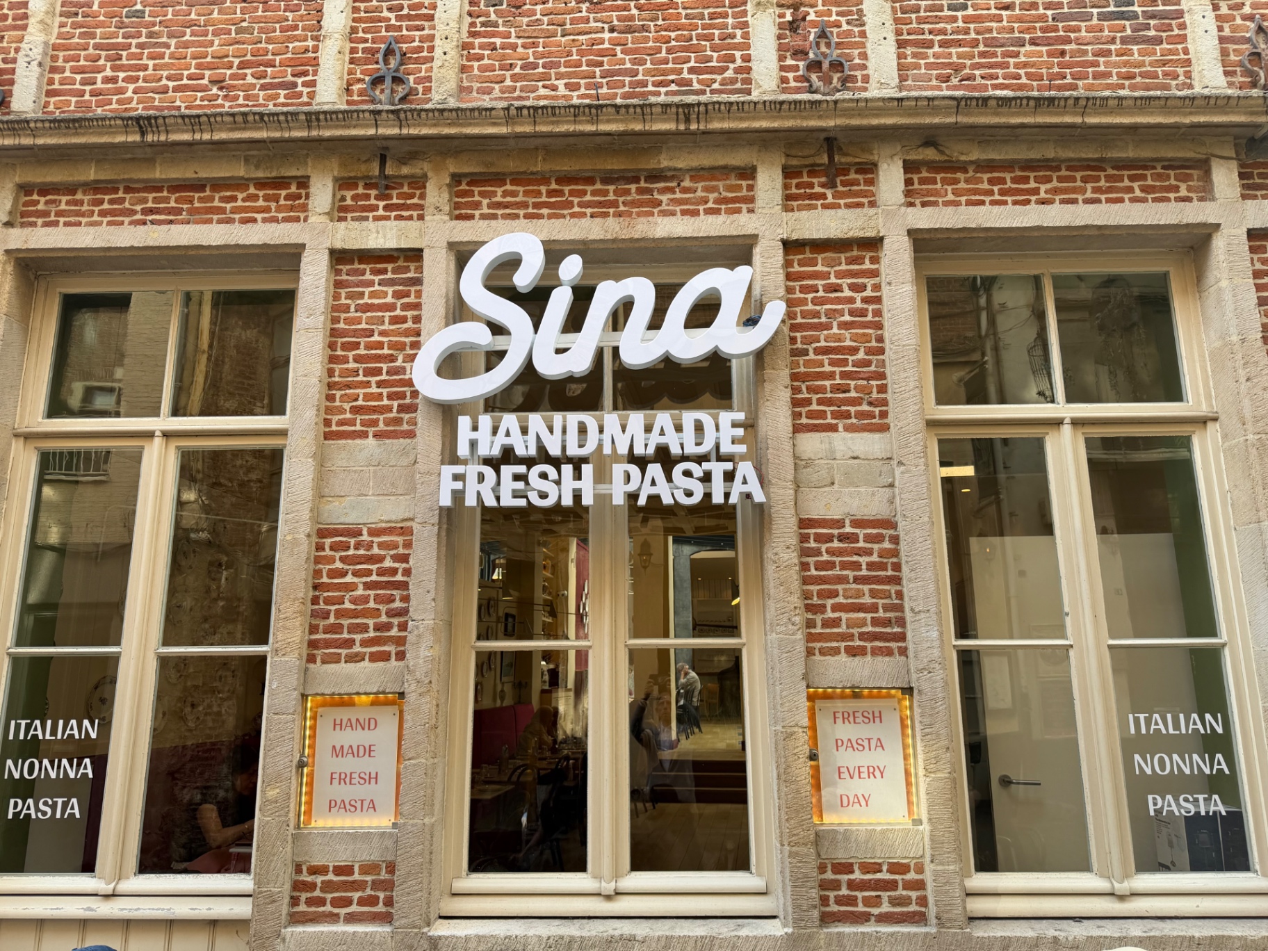 Pâtes fraîches au pesto de pistache et burrata, dressées devant la cuisine ouverte. © BXLOVE Enseigne Sinamisu, lettres dorées et lanternes, Galerie du Roi à Bruxelles