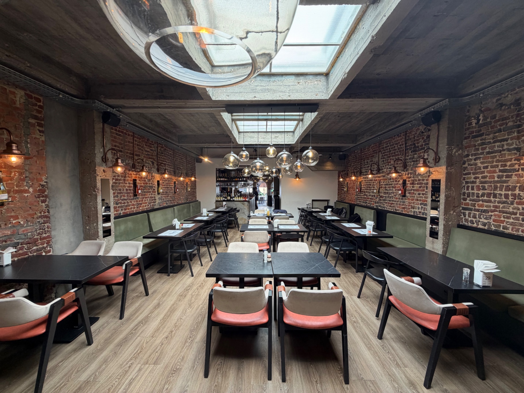 Salle intérieure de Pescobar Brussels : briques rouges, banquettes vertes, suspensions en verre, parquet clair