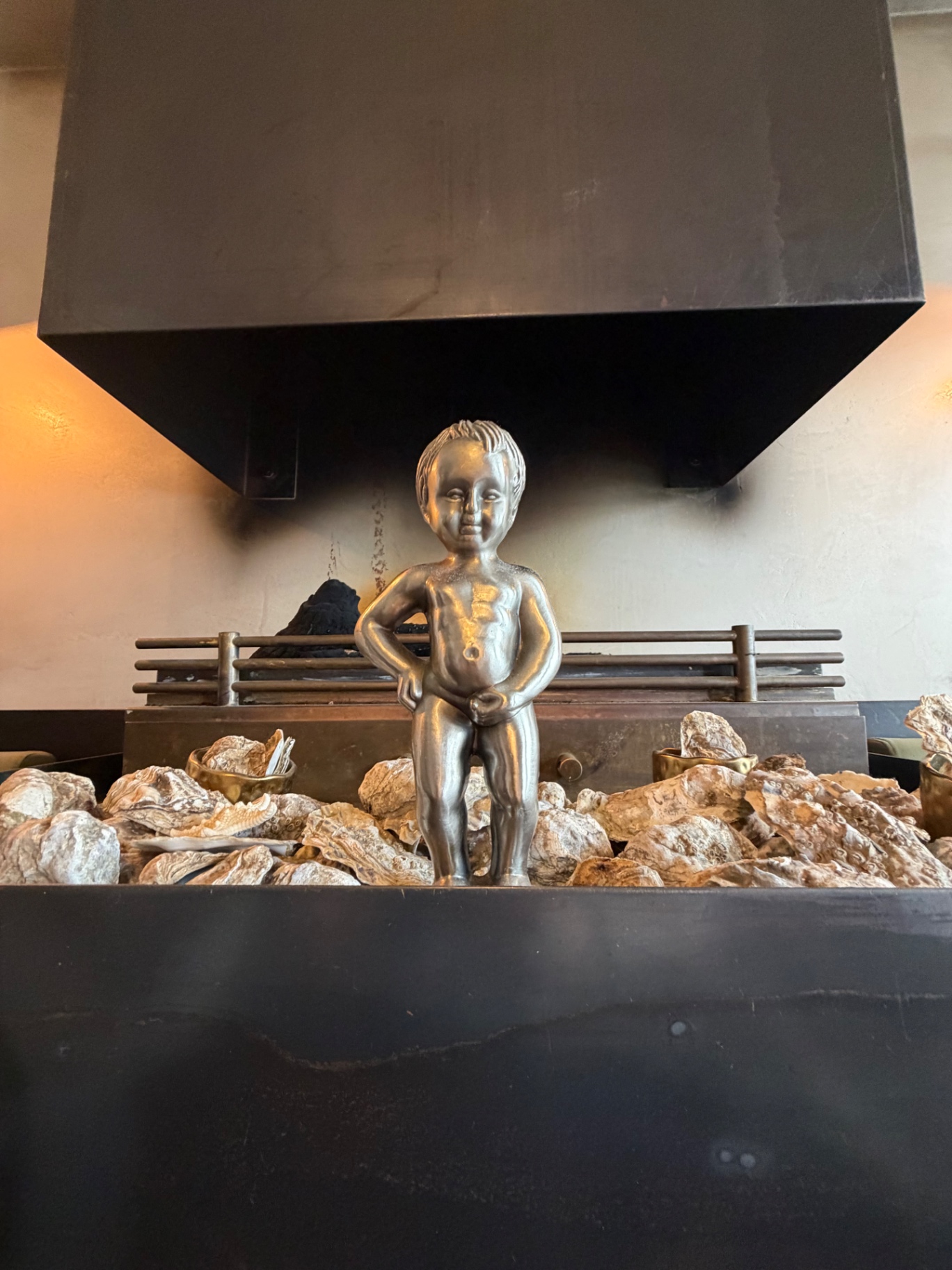 Statue du Manneken-Pis en bronze posée sur un lit de coquilles d’huîtres devant le four à braise du Pescobar Brussels