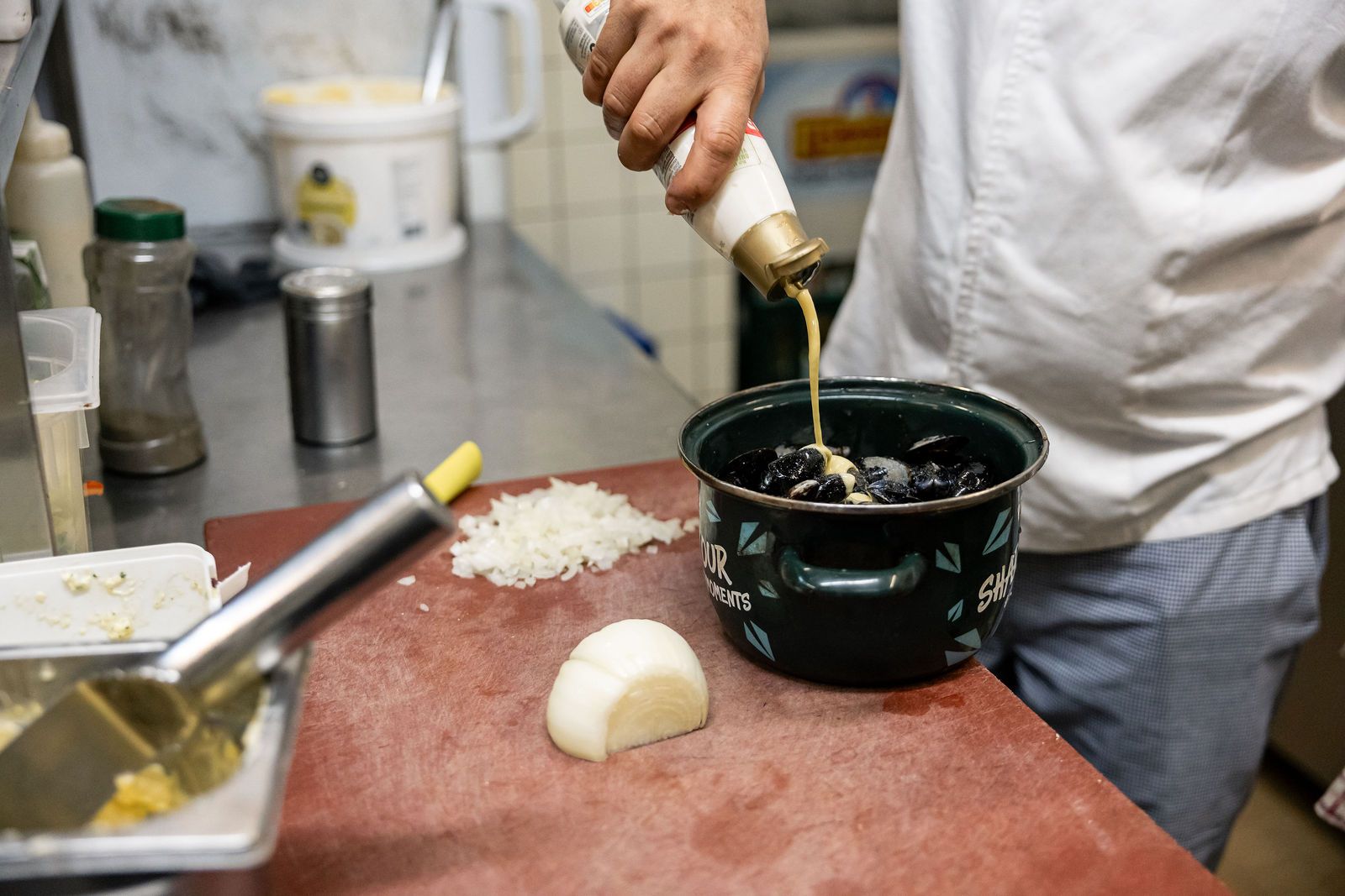 Le cuisinier arrose les moules dans une casserole émaillée verte